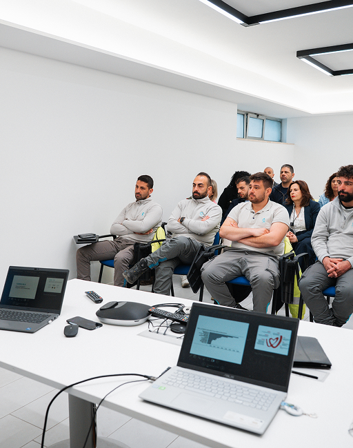 Sala gremita durante la sessione formativa: il relatore a sinistra indica lo schermo, davanti a lui i partecipanti seduti in più file.