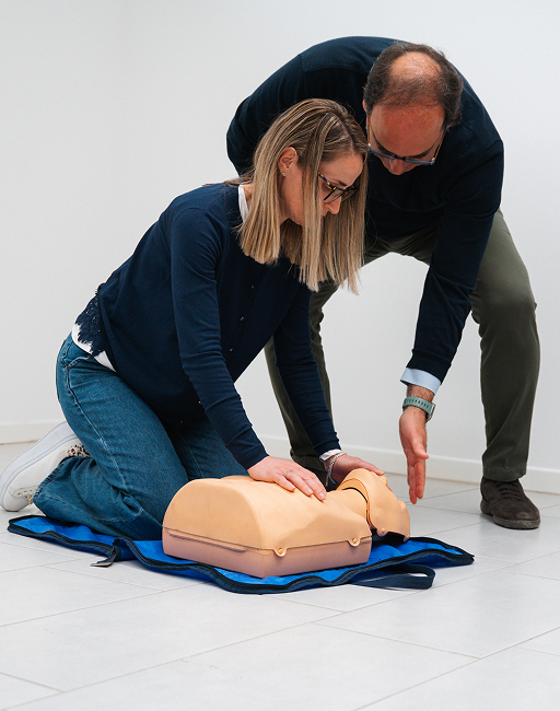 Una partecipante prova il massaggio cardiaco su un manichino, guidata dal formatore che le indica il punto corretto delle compressioni.